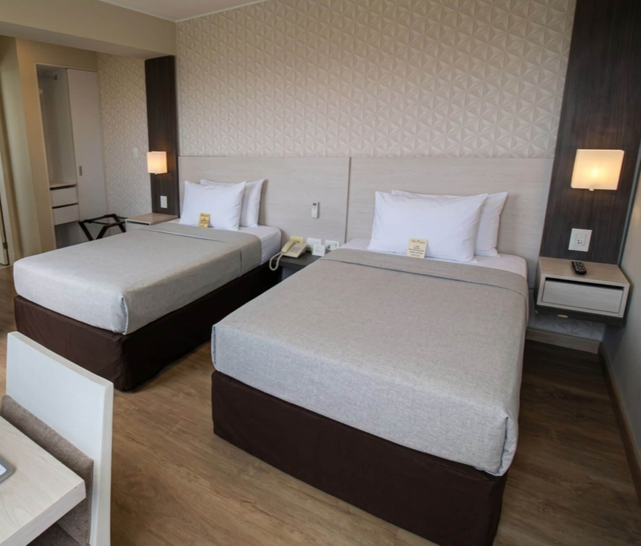 A hotel room with two beds, a desk, a chair, a phone, and a lamp.