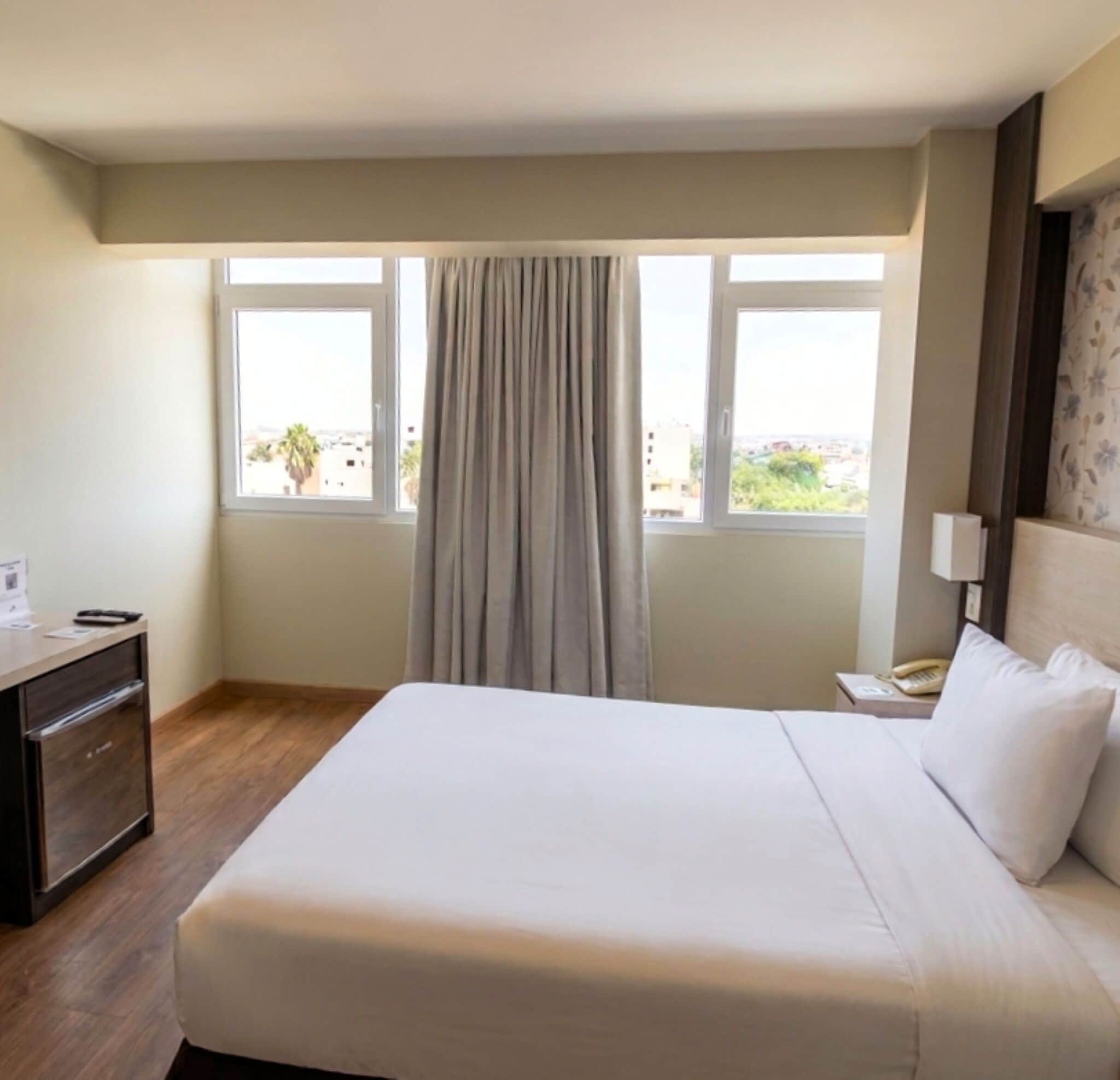 Une chambre d’hôtel avec un lit, un bureau, un téléphone et une fenêtre avec des rideaux.