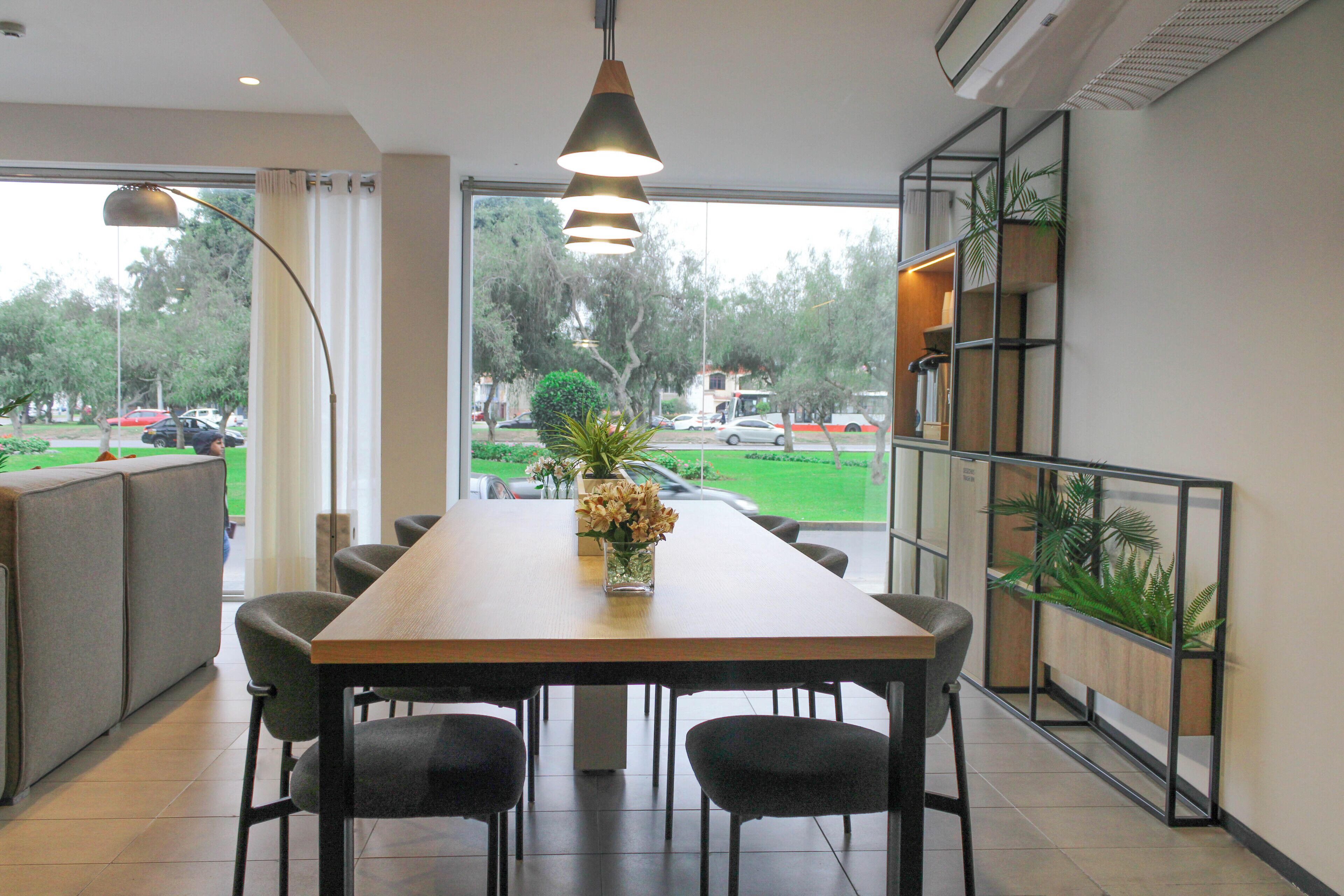 A dining area with a long table, chairs, a vase of flowers, and a view of the outdoors.