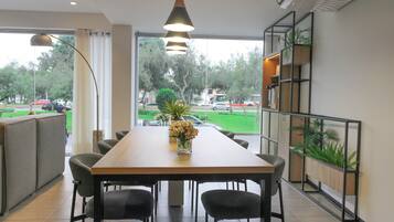 A dining area with a long table, chairs, a vase of flowers, and a view of the outdoors.