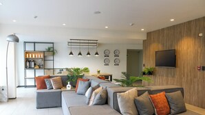 A modern living room with a sectional sofa, a flat-screen TV, pendant lights, and a kitchen area in the background. - Palmetto Hotel Business San Miguel (Lima)