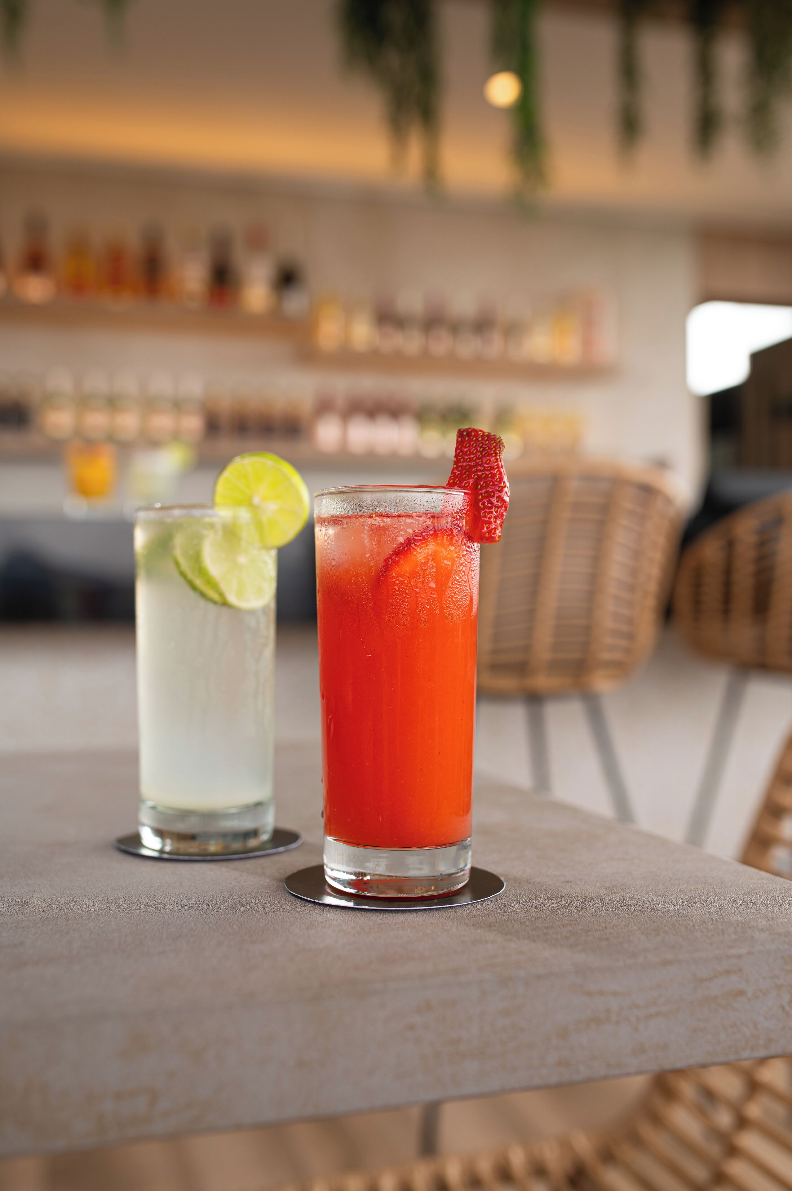 Two glasses of iced drinks on a table with a wicker chair in the background.