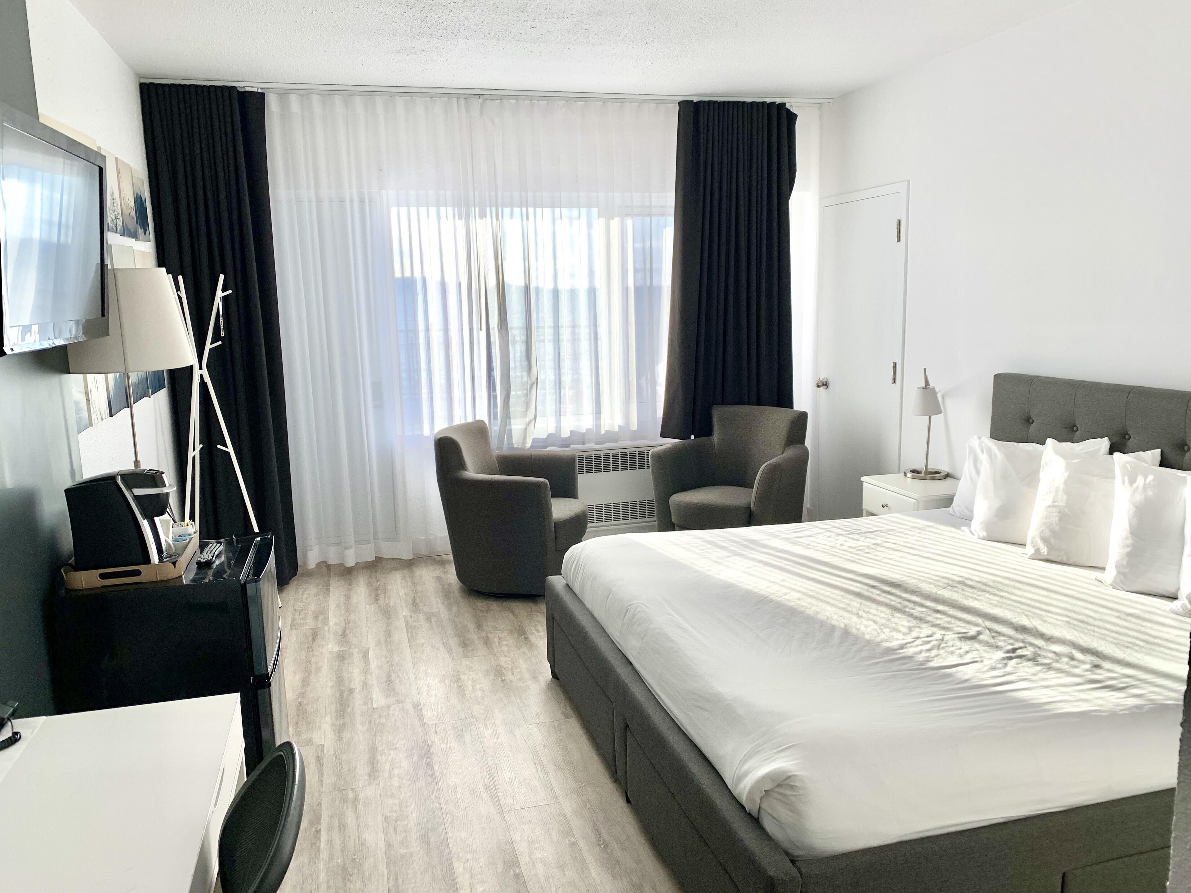 A hotel room with a bed, a desk, a chair, a TV, and a window with curtains.