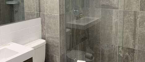 Un baño moderno con ducha de vidrio, inodoro blanco y lavamanos.