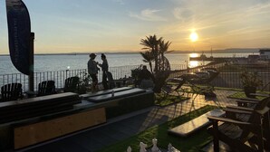Un patio frente al agua con asientos al aire libre, una bandera y vistas al atardecer sobre el mar.