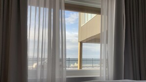 Habitación de hotel con una cama grande, cortinas translúcidas y vistas a un edificio y una masa de agua.