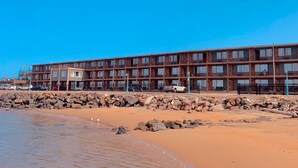 Un hotel de varios pisos con fachada de piedra, ubicado junto a una playa de arena.