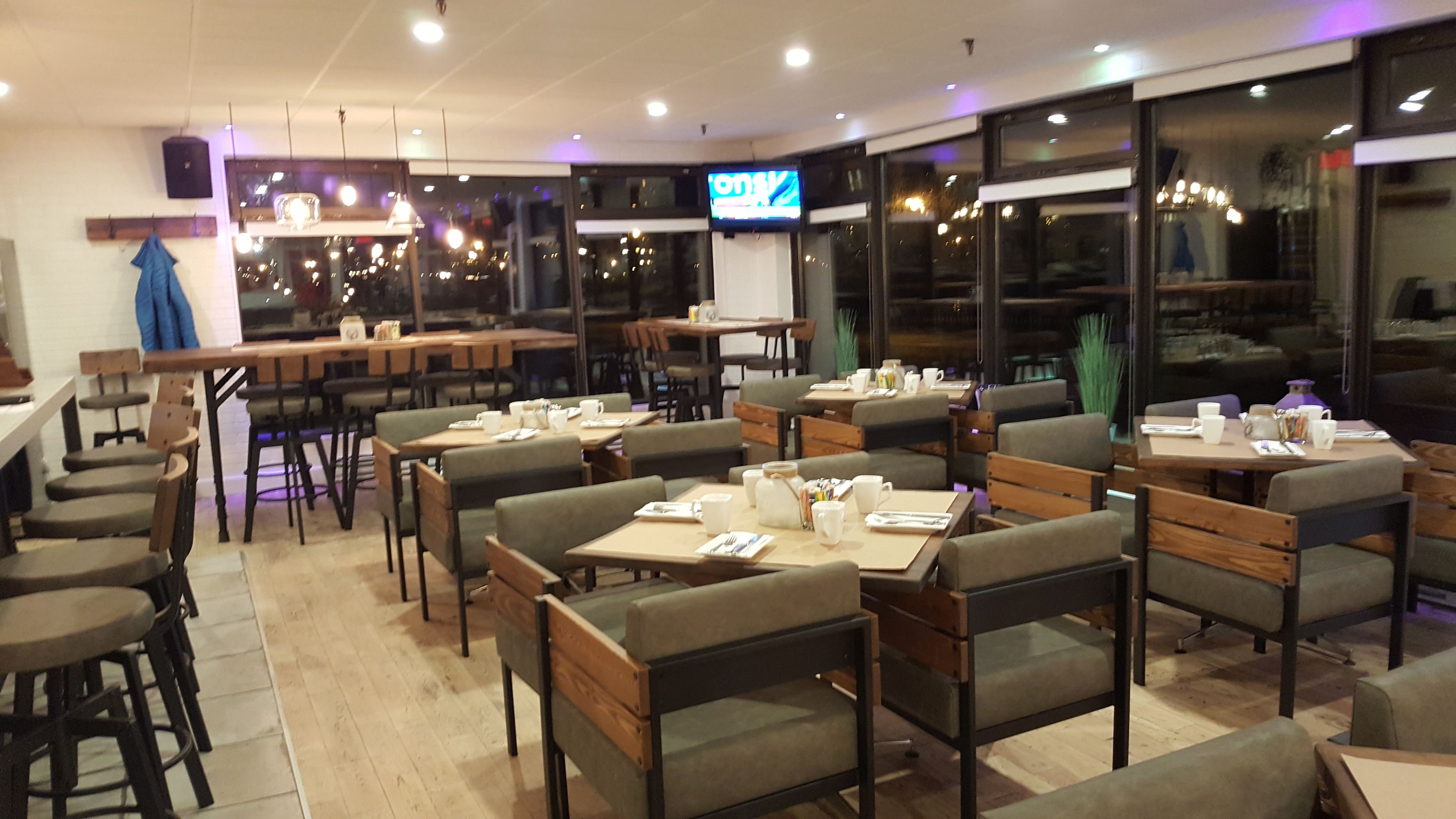 Een restaurant met meerdere tafels en stoelen, een televisiescherm en grote ramen.
