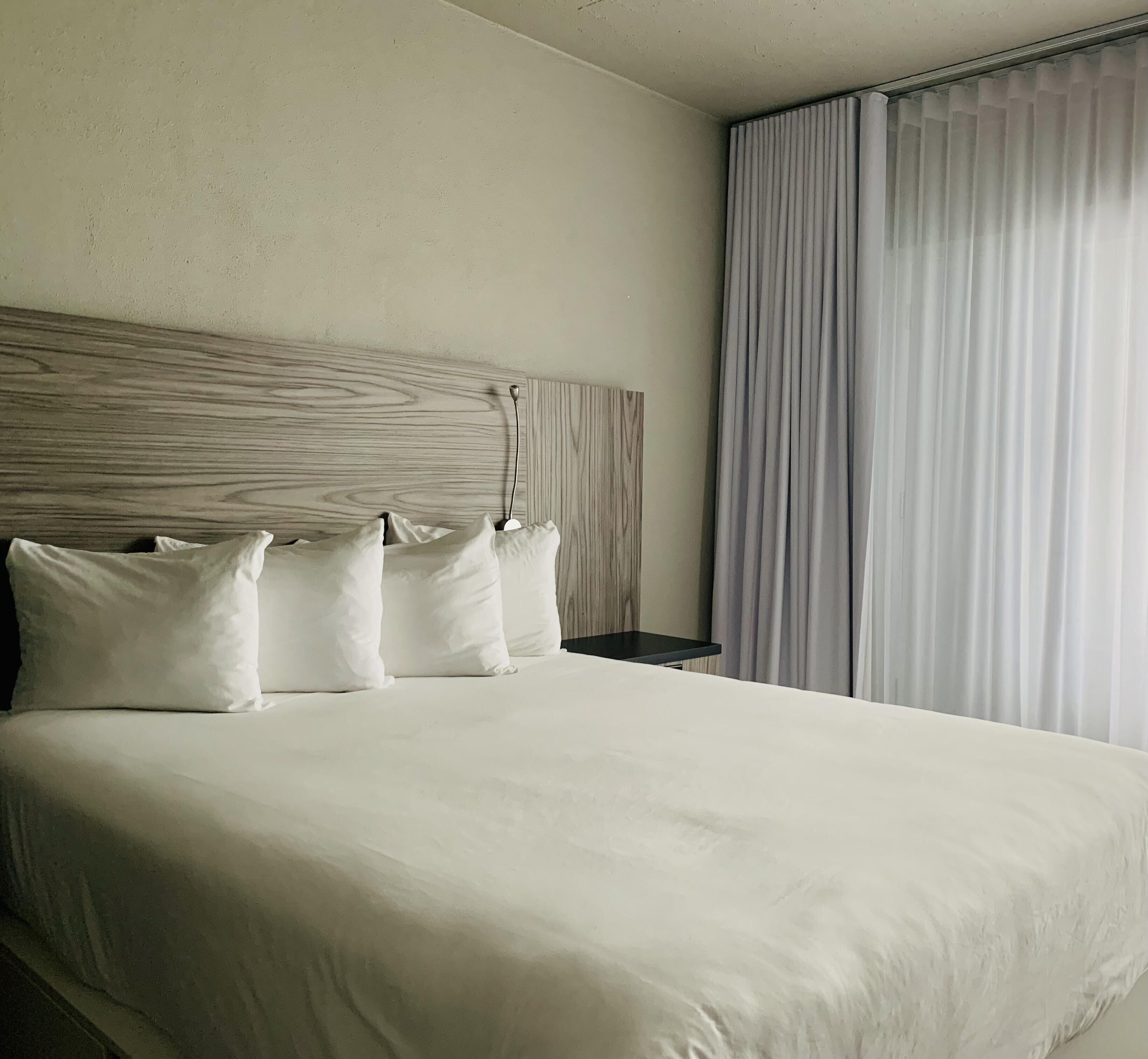 Una cama bien hecha con cabecera de madera, almohadas blancas y una mesita de noche con lámpara.