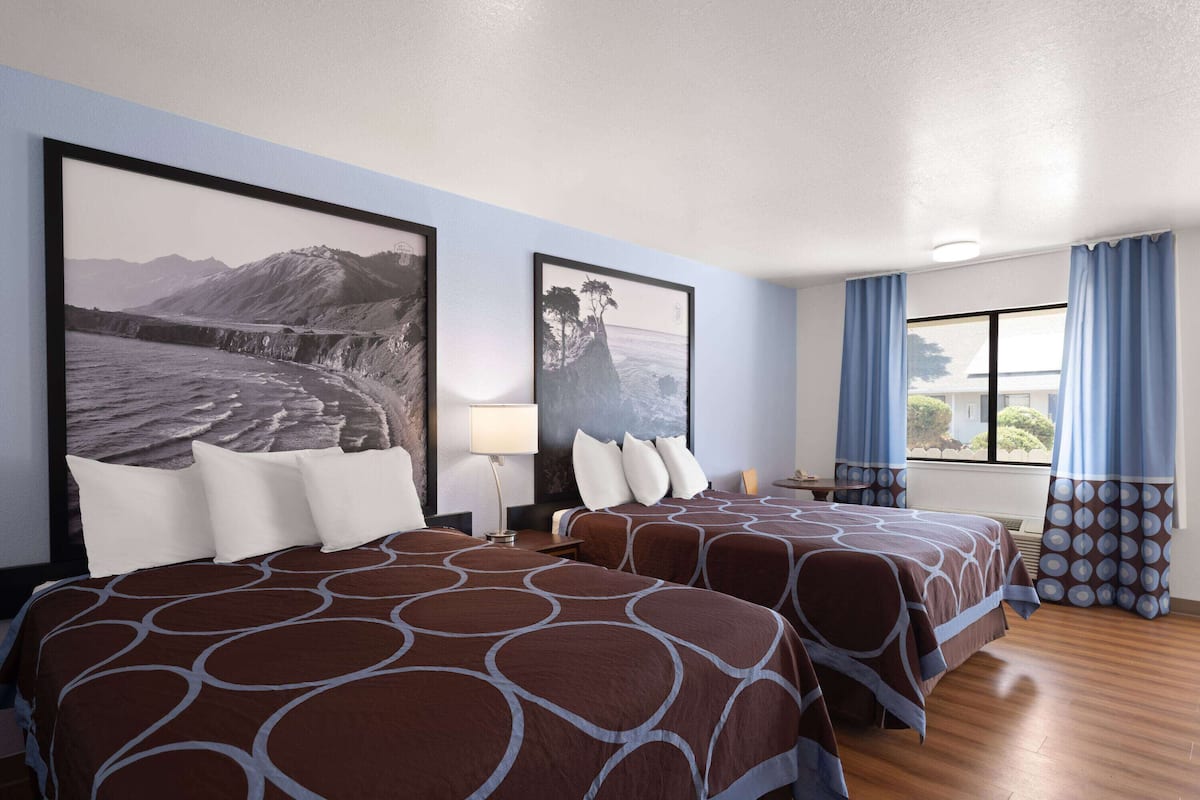 Habitación de hotel con dos camas, un ventanal con cortinas y obras de arte en las paredes.