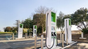 A row of electric vehicle charging stations with a clear road and trees in the background.