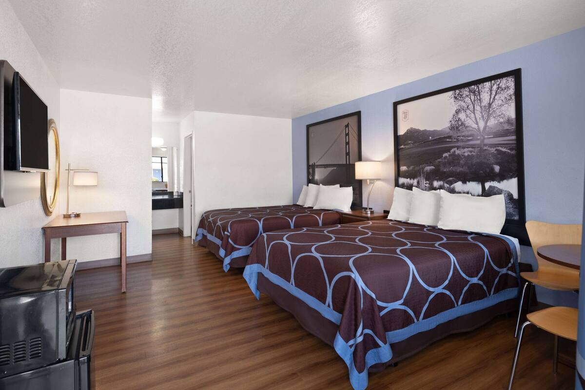 Una habitación de hotel con dos camas, un escritorio, un televisor y obras de arte en las paredes.