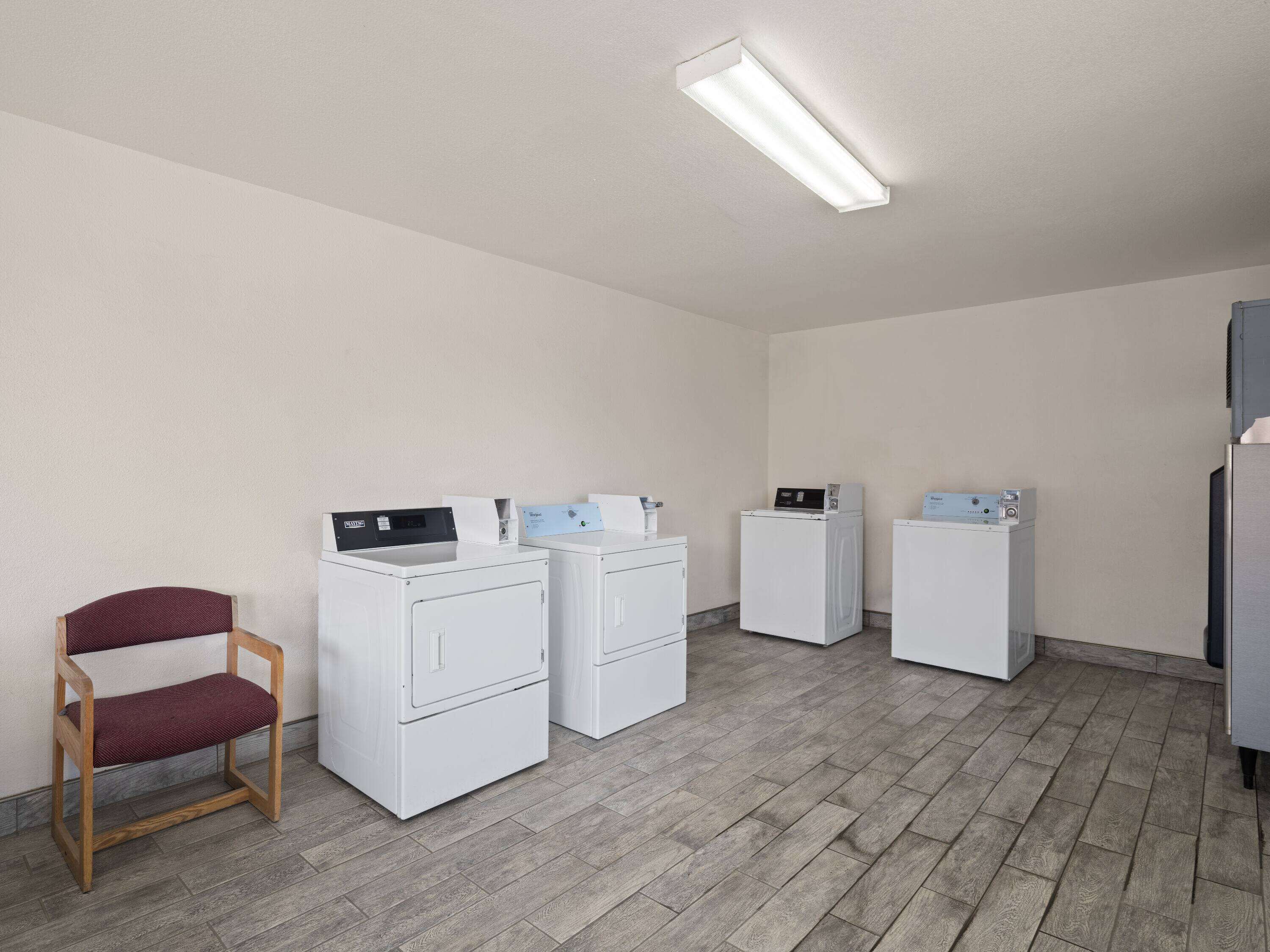 A laundry room with four white washing machines, a wooden chair, and a fluorescent light fixture.
