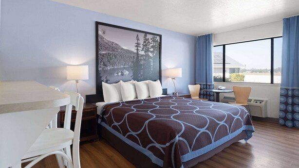 A hotel room with a bed, a desk, and a chair. There is a window with curtains and a view of the outside.
