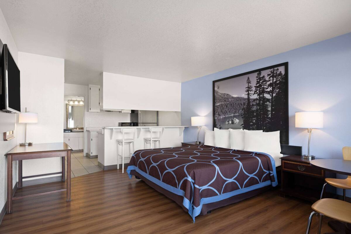 Habitación de hotel con cama, escritorio, silla, kitchenette pequeña y ventana grande.