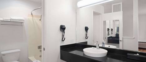 Un baño moderno con inodoro blanco, lavamanos negro y dos secadores de pelo montados en la pared.