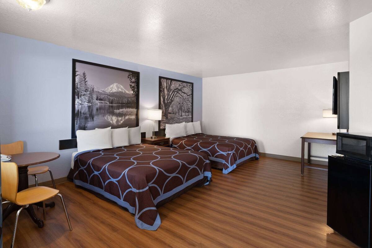 Habitación de hotel con dos camas, un escritorio, una silla, un televisor y dos cuadros en la pared.