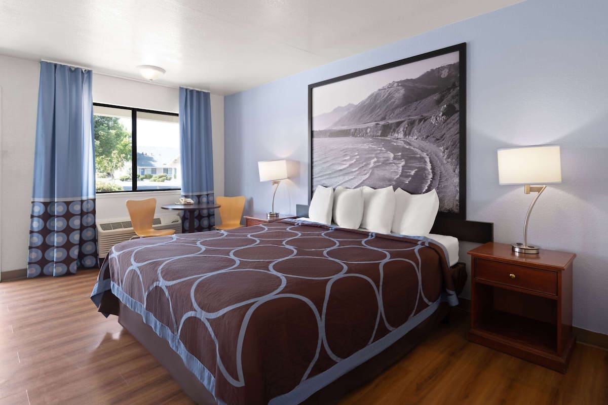 Habitación de hotel con una cama grande, dos mesitas de noche, una ventana con cortinas y un cuadro grande en la pared.
