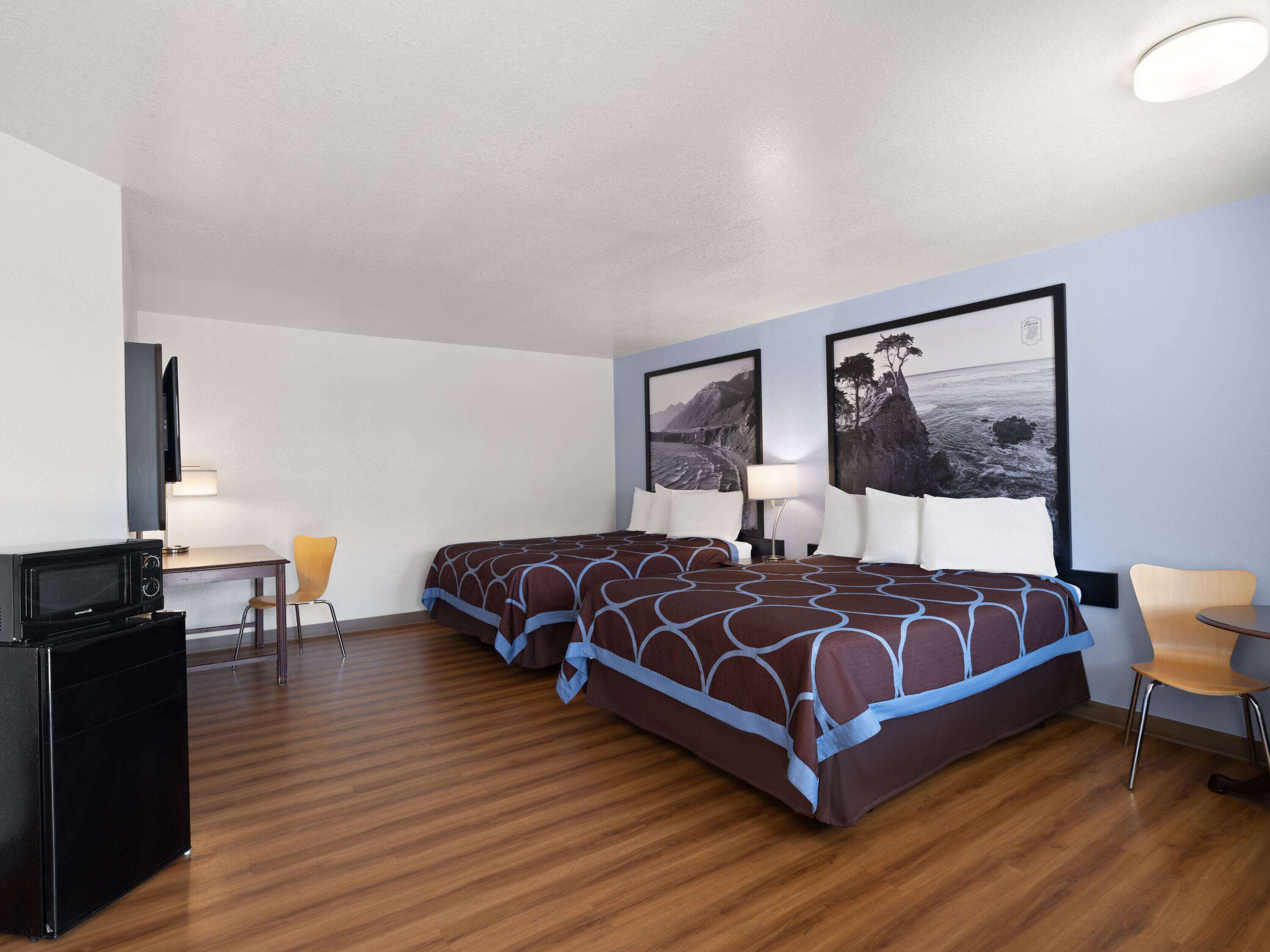 Une chambre d’hôtel avec deux lits, un bureau, une télévision et deux chaises.