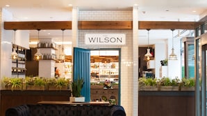 Un interior acogedor con un banco tapizado oscuro, vigas de madera y un letrero que dice "THE WILSON".