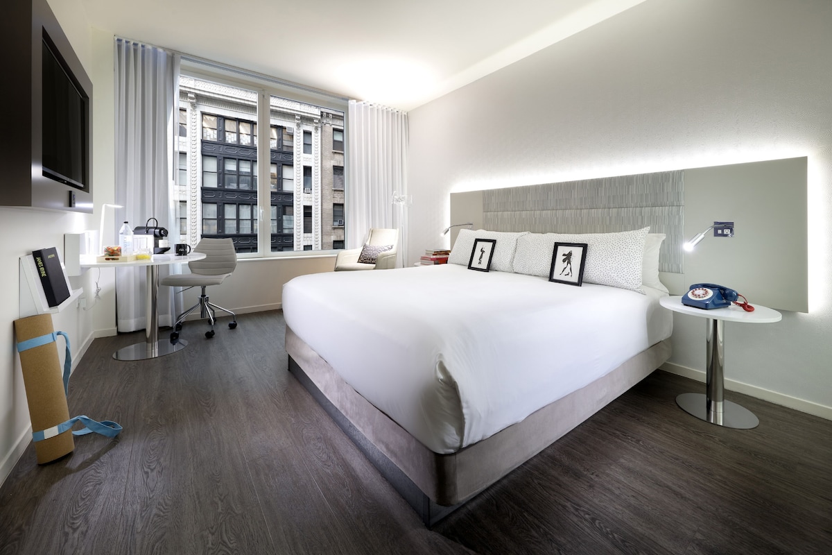 A hotel room with a large bed, a desk with a chair, a TV, and a window with curtains.