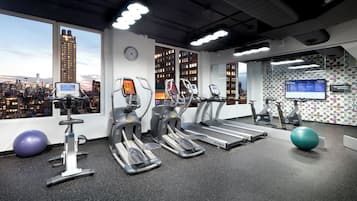 A gym with treadmills, elliptical machines, and exercise balls, with a cityscape view through large windows.
