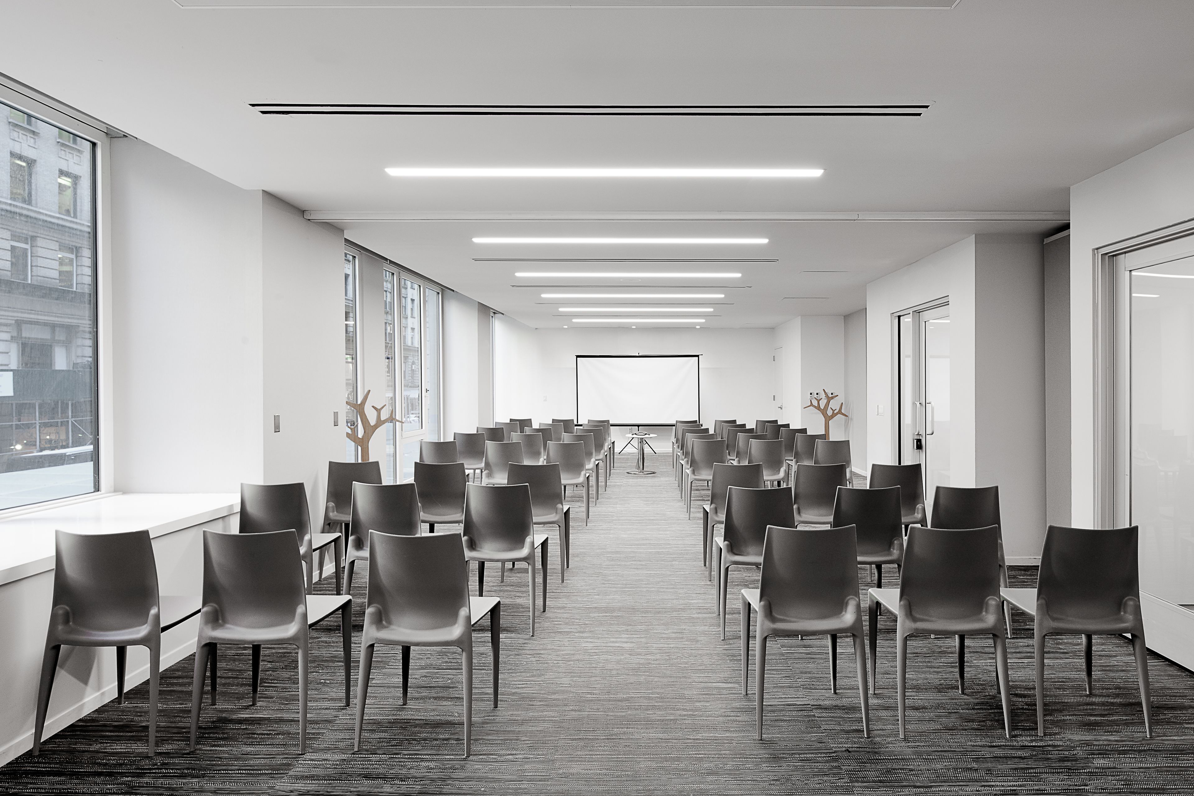 A conference room with rows of chairs, a projector screen at the front, and large windows on one side.