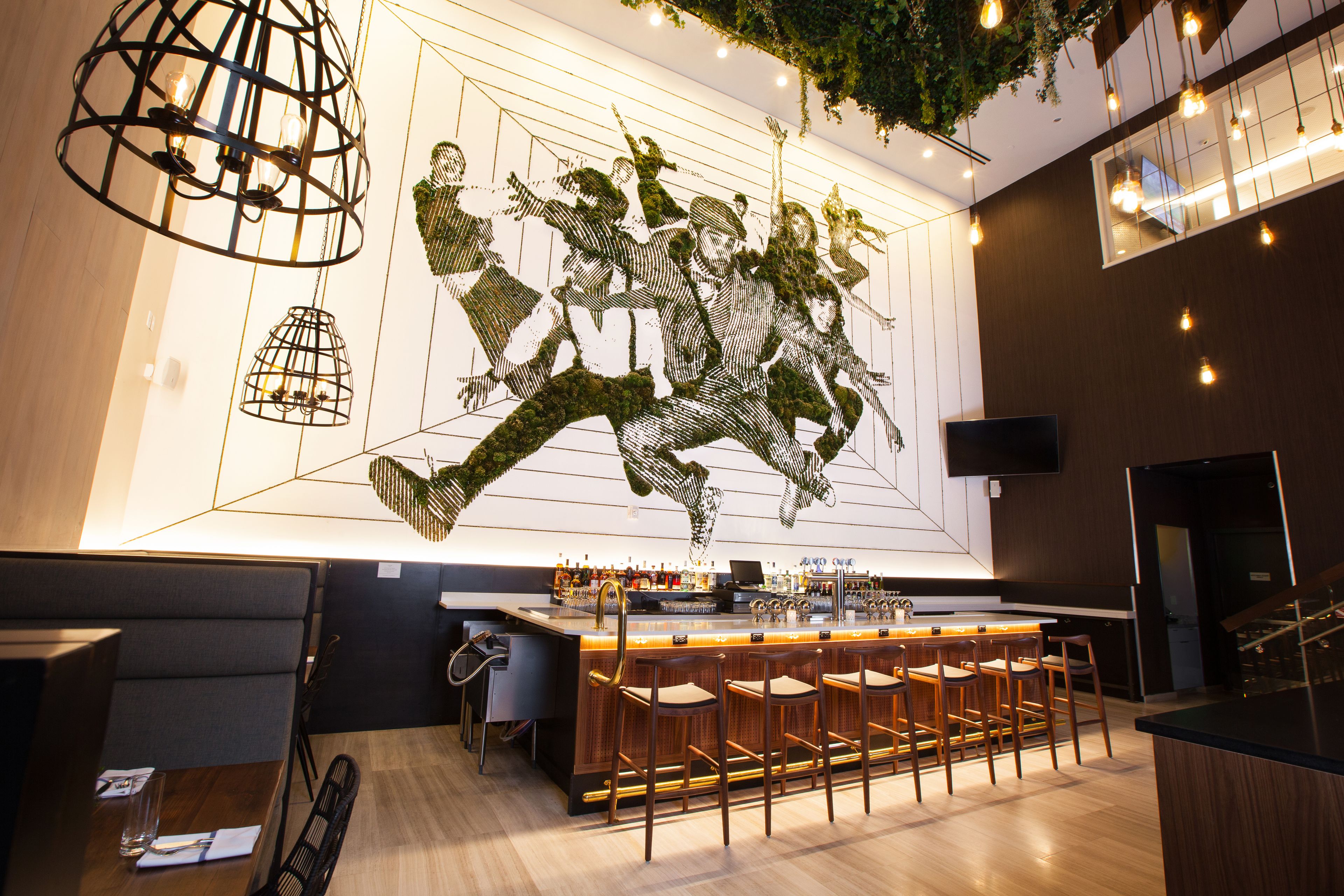Un área de bar moderna con una barra larga, taburetes y un mural grande en la pared.