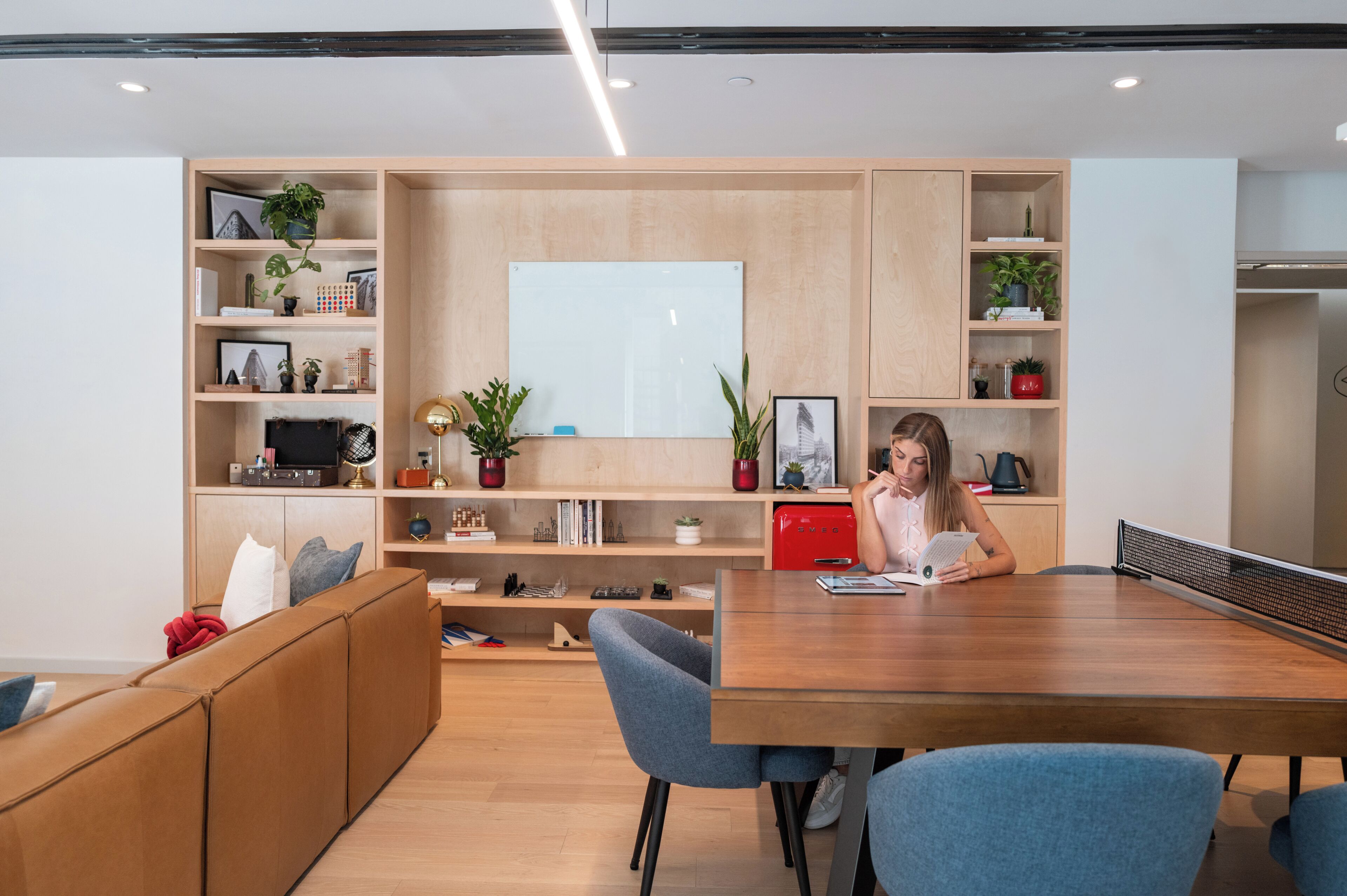Um espaço de escritório moderno com escrivaninha de madeira, cadeiras azuis e estantes com plantas e livros.