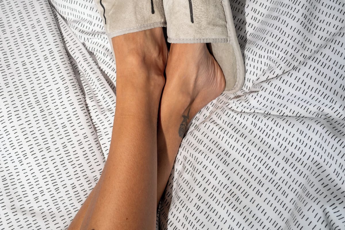 A bed with a patterned bedspread and a pair of light-colored slippers.