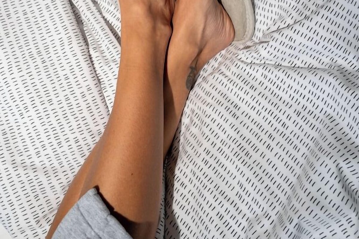 A bed with a patterned bedspread and a pair of light-colored slippers.
