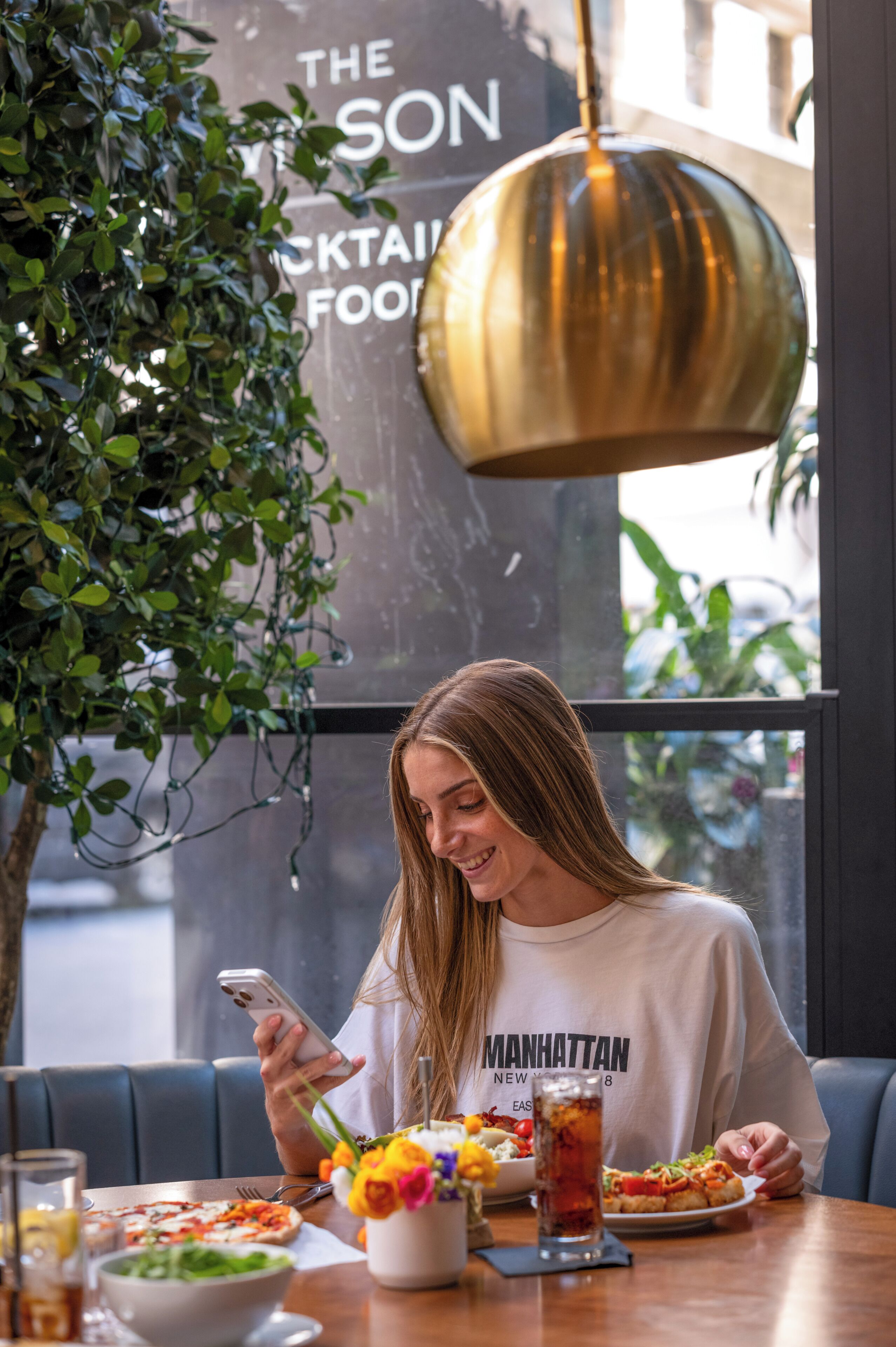 Une personne assise à une table, avec un téléphone intelligent, un saladier rempli de salade, une assiette de nourriture et une boisson.