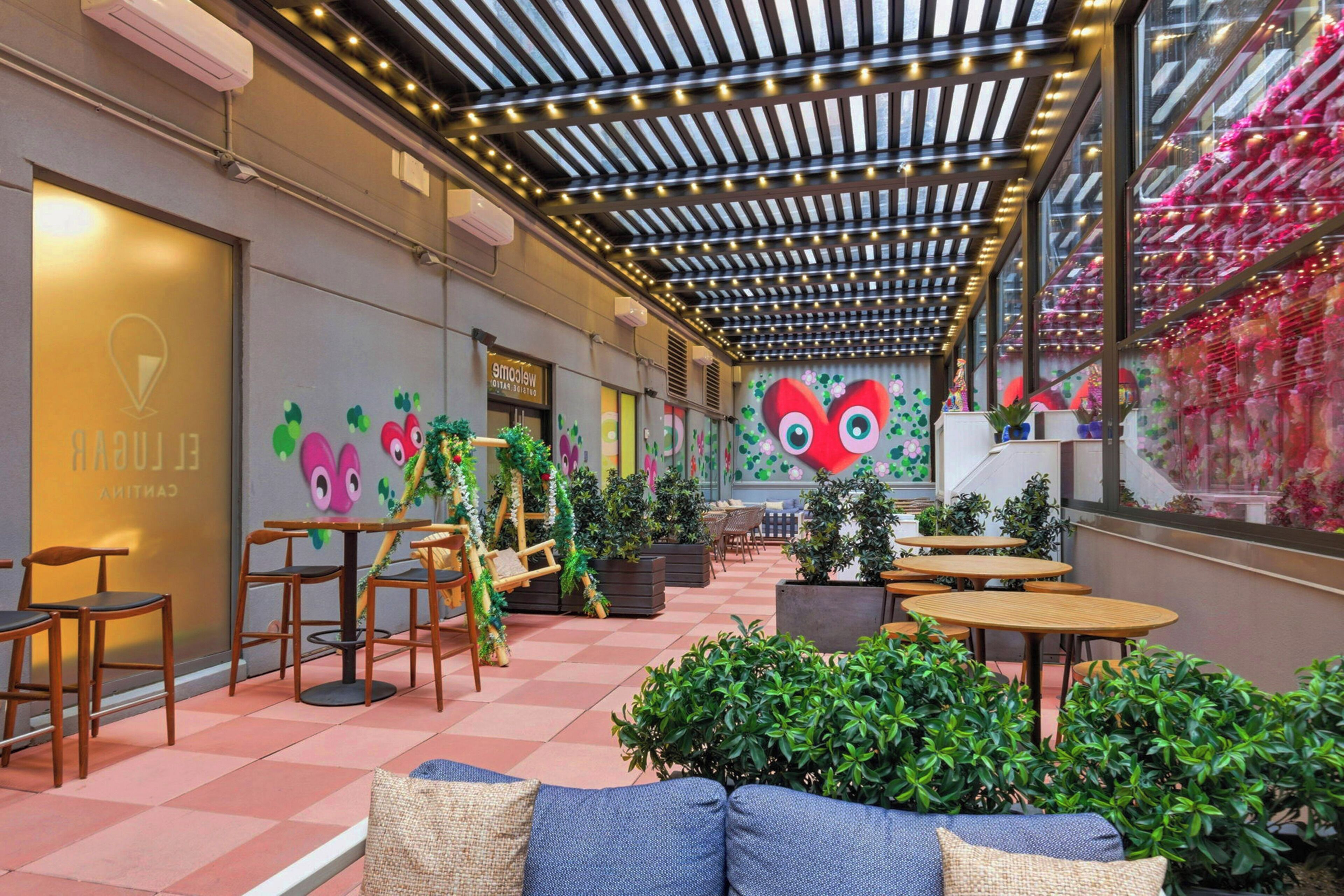 Un café avec des tables et des chaises en bois, des plantes en pot et une fresque colorée sur le mur.