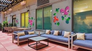 A modern outdoor seating area with sofas and a table, surrounded by large windows and decorative wall art.
