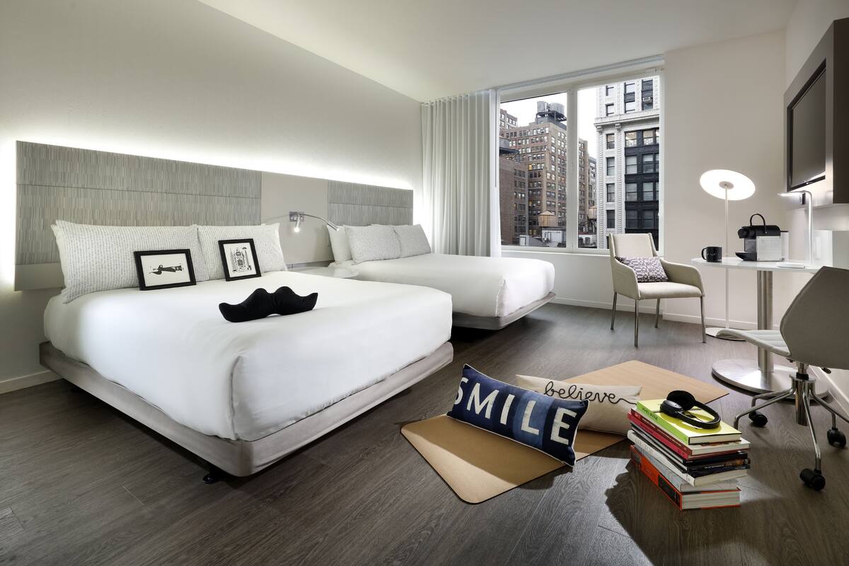 A hotel room with a large bed, a desk, a chair, and a view of the city.