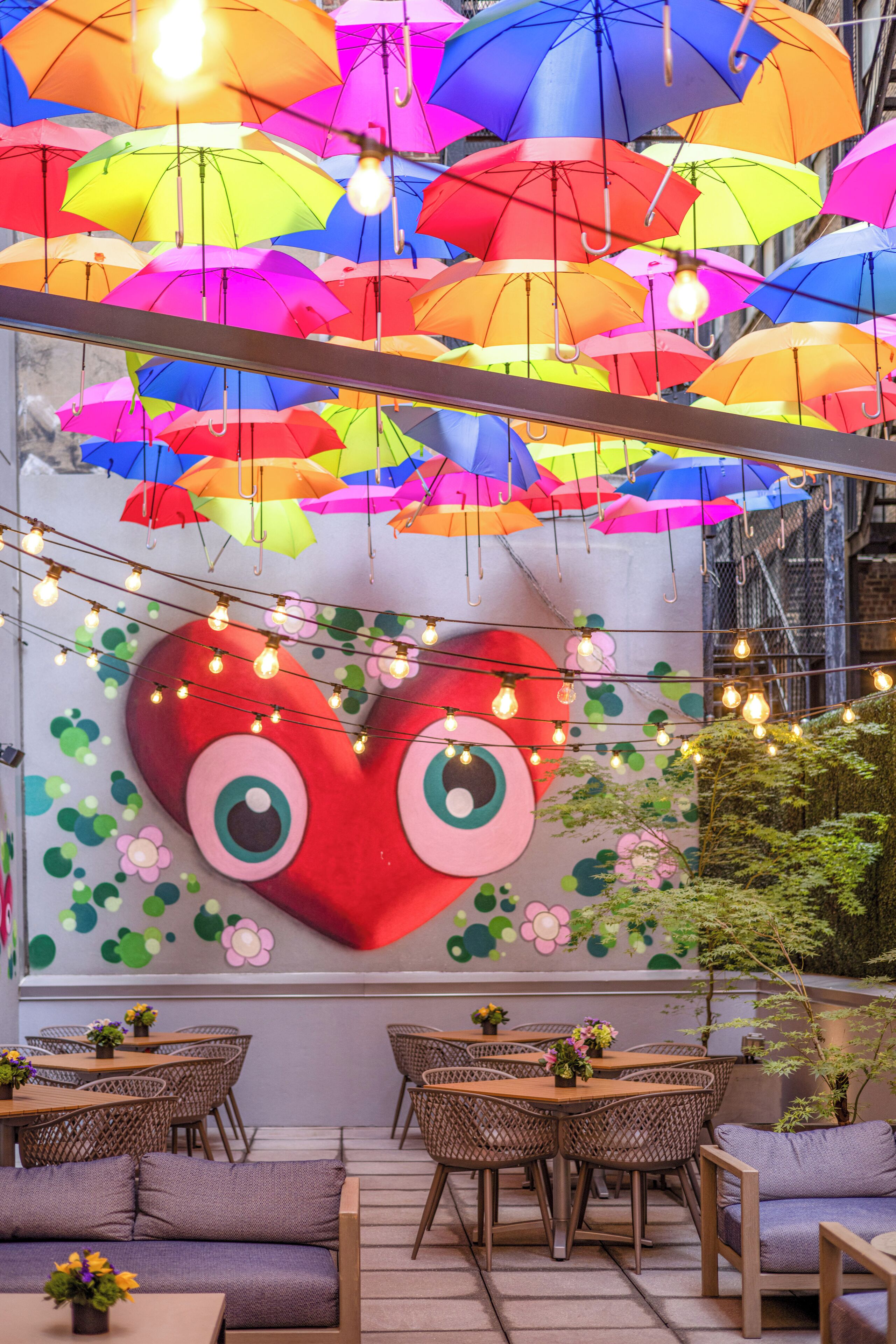 A restaurant with outdoor seating, colorful umbrellas, and a large heart-shaped mural.