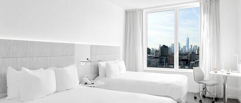 Habitación de hotel con dos camas, un escritorio y vistas a un horizonte urbano.