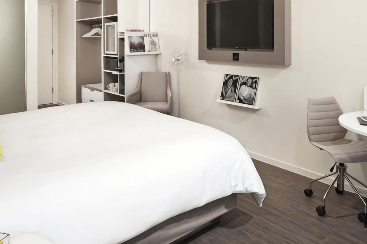 A hotel room with a bed, a desk, a chair, a TV, and a wardrobe.