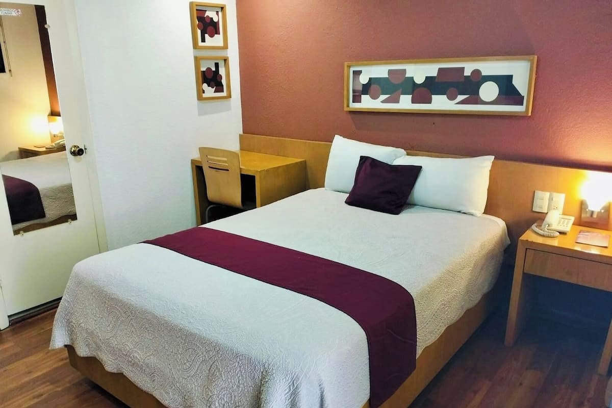 A hotel room with a bed, bedside table, lamp, and a door with a mirror.