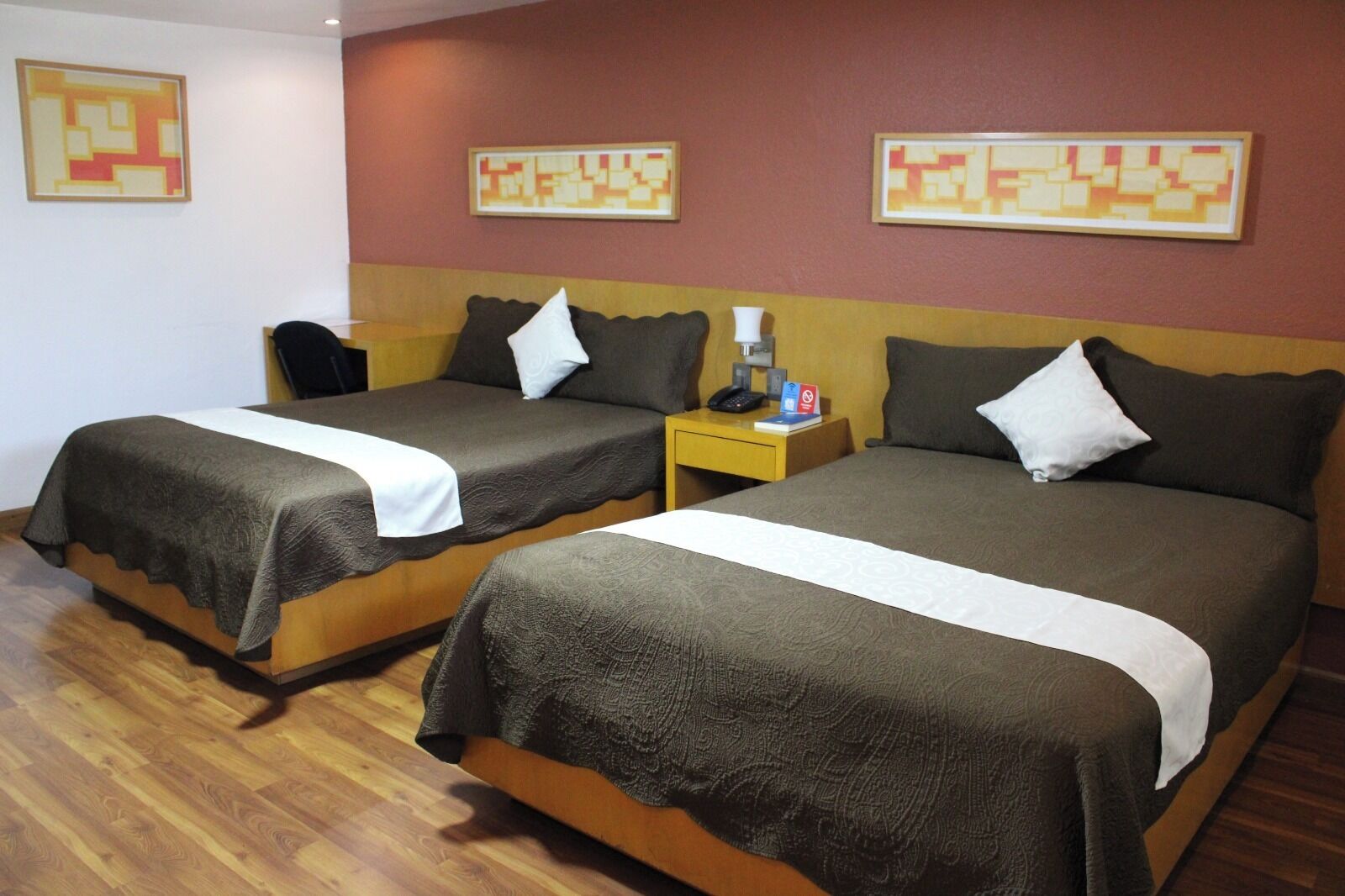 A hotel room with two beds, wooden flooring, and artwork on the walls.