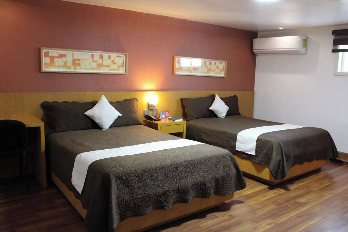 A hotel room with two beds, a nightstand, a lamp, and an air conditioning unit.