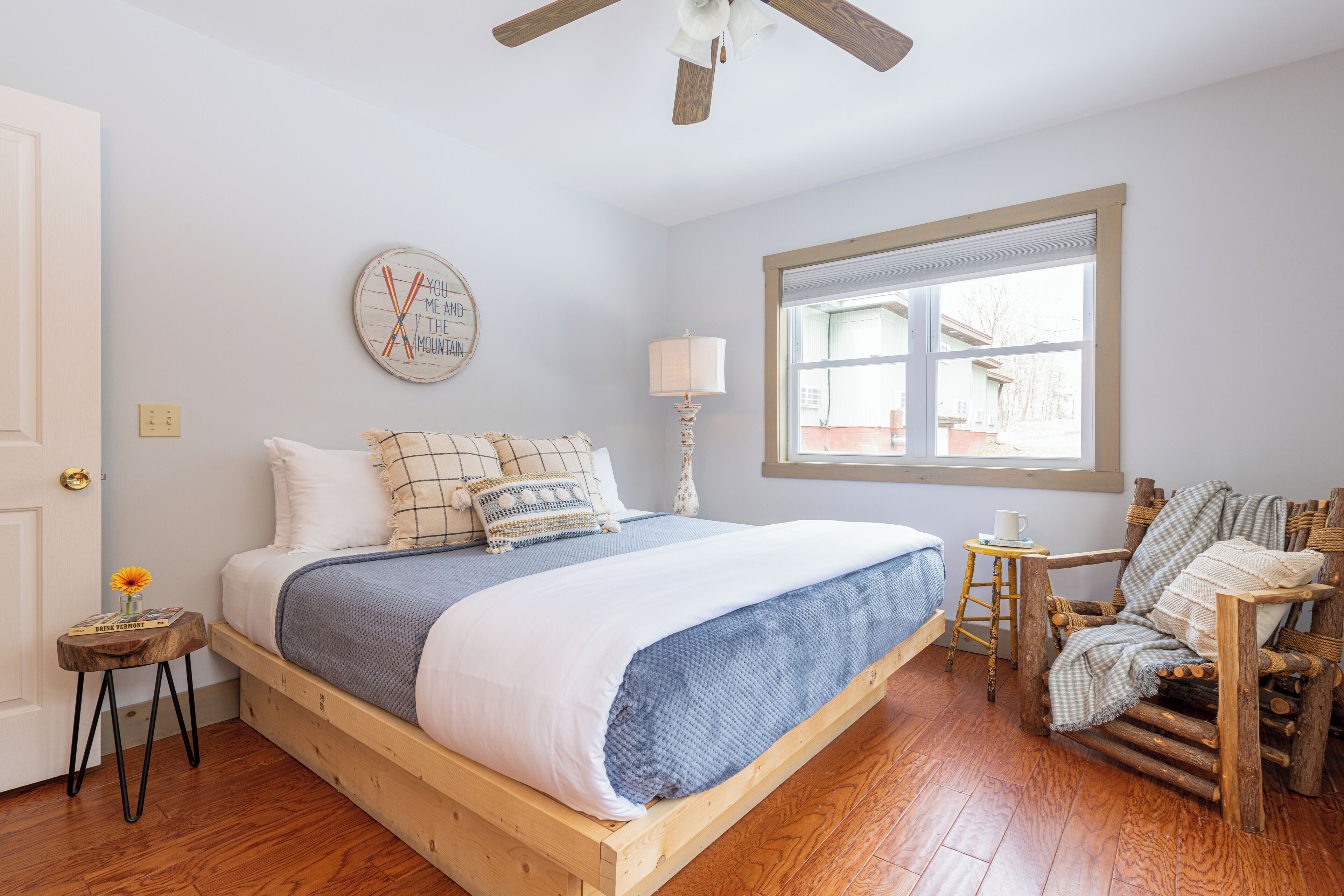 A bedroom with a wooden bed, a window with a view, a lamp, and a chair.
