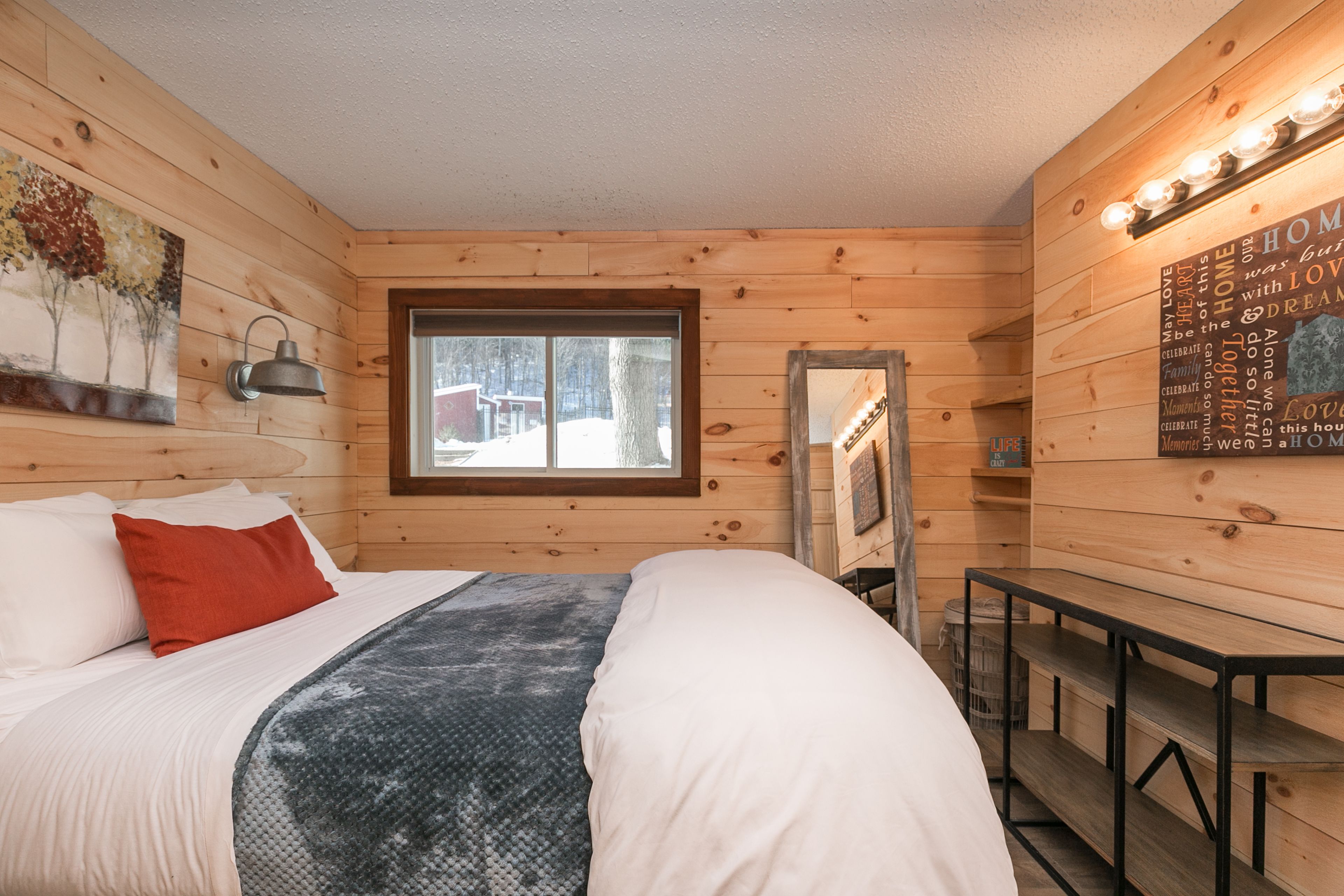 Ein gemütliches Cabin-Zimmer mit Bett, Fenster, Schreibtisch und einer Wand mit Leuchte und Poster.