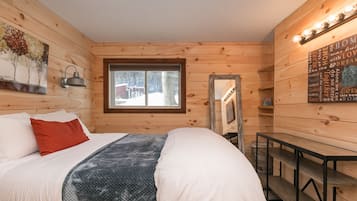 Ein gemütliches Cabin-Zimmer mit Bett, Fenster, Schreibtisch und einer Wand mit Leuchte und Poster.
