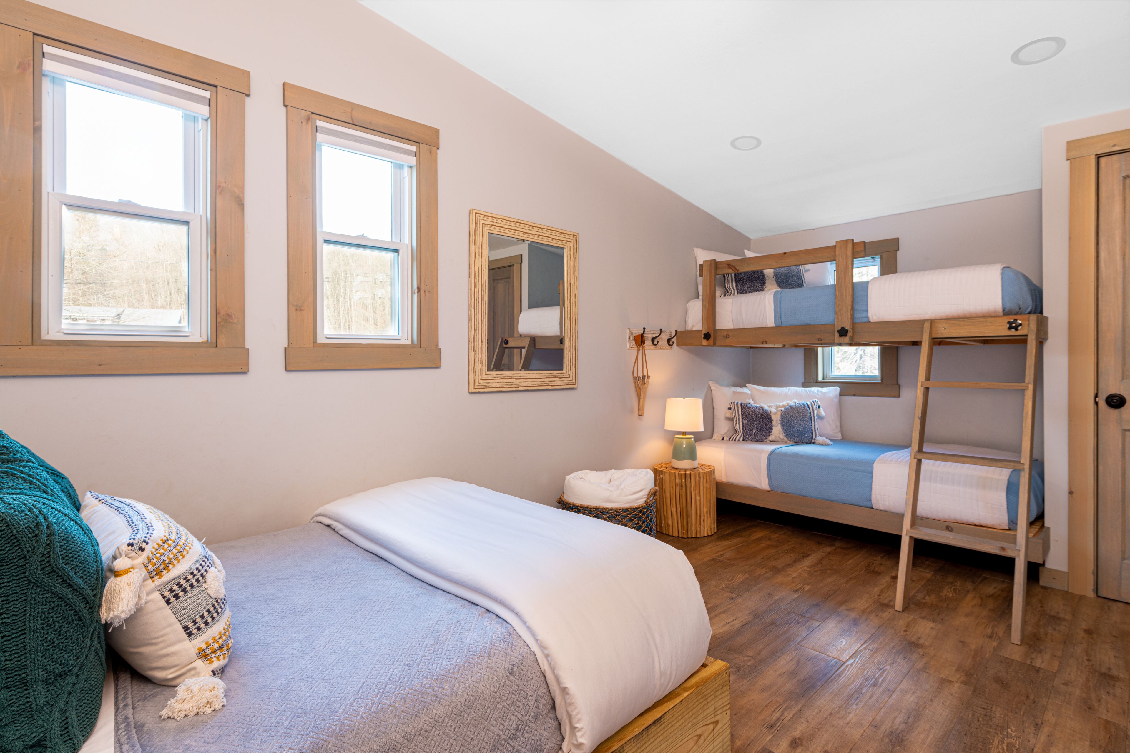 A cozy bedroom with a bunk bed, a single bed, a mirror, and a small bedside table with a lamp.