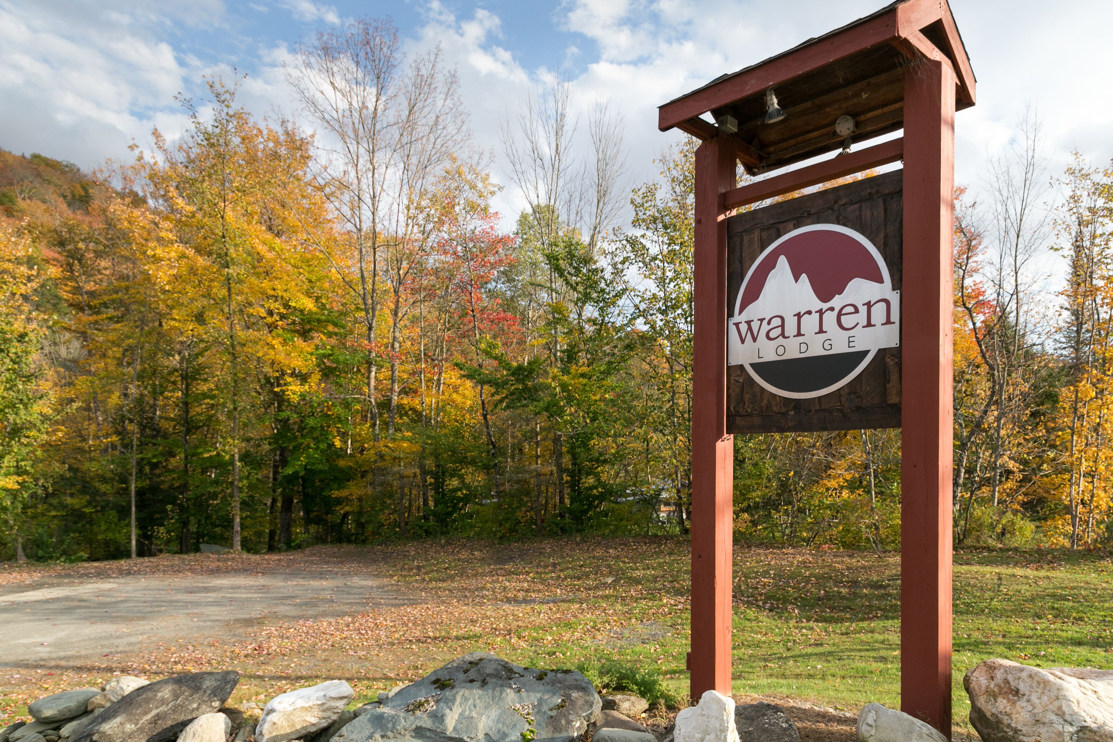 A wooden sign with the text "warren lodge" and a mountain graphic, set against a backdrop of autumn-colored trees.