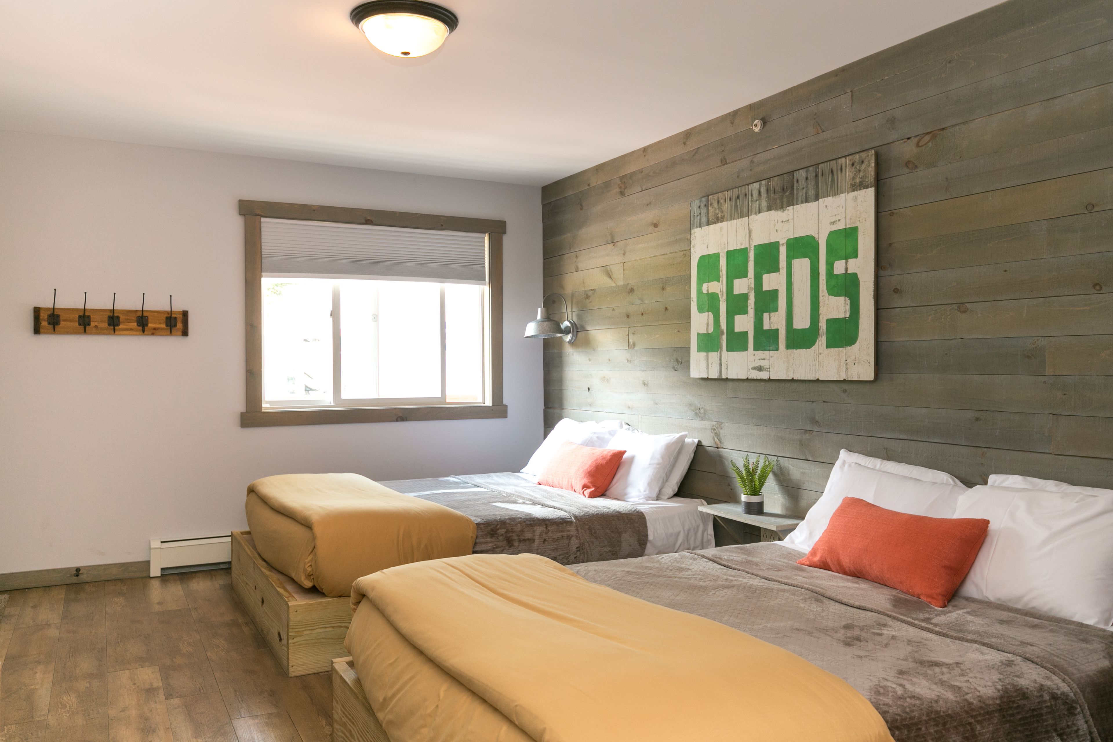 Un dormitorio con dos camas, una ventana, un cartel en la pared y una planta pequeña.