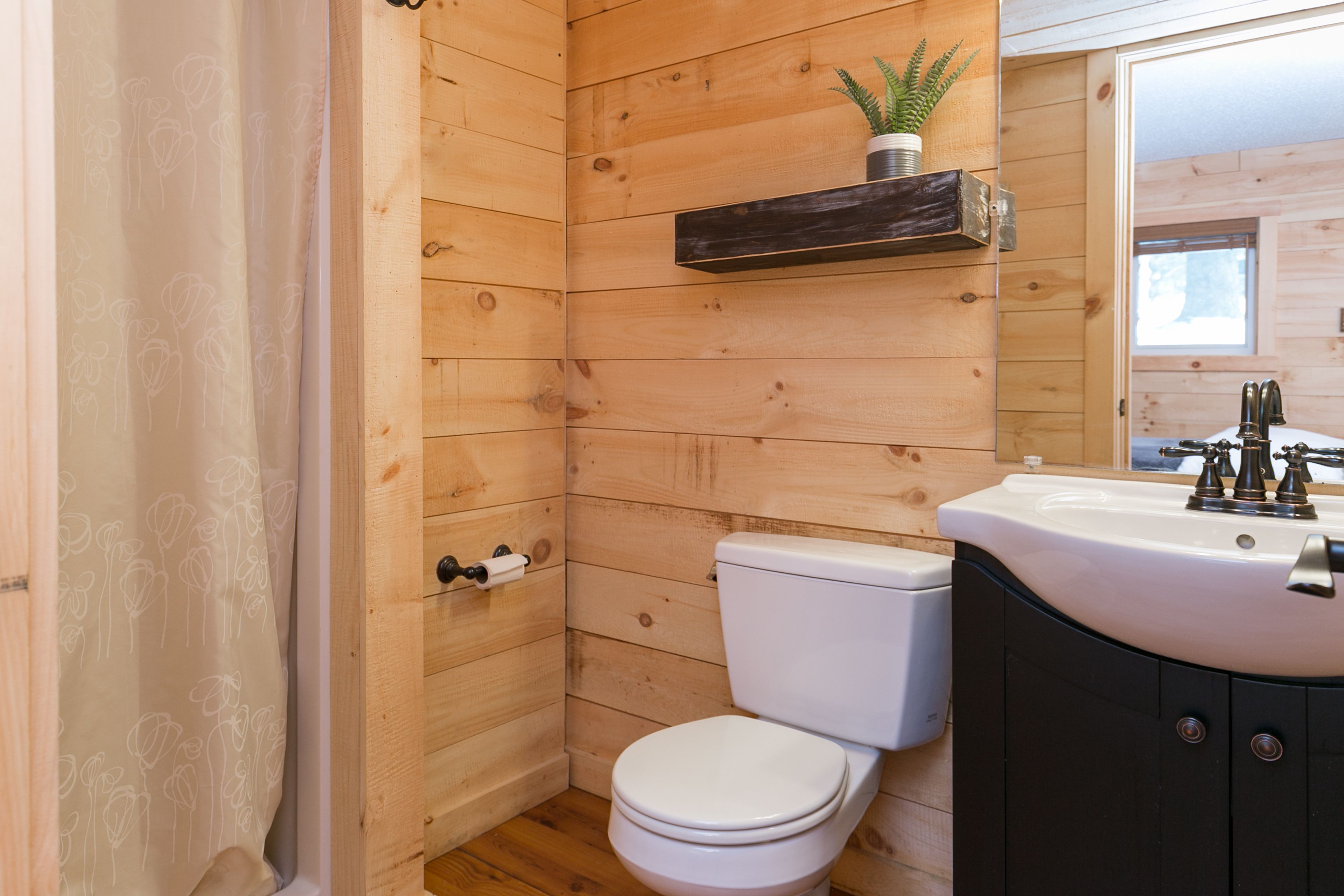 Un baño con paneles de madera, un inodoro blanco, un lavabo con espejo y un estante pequeño con una planta.