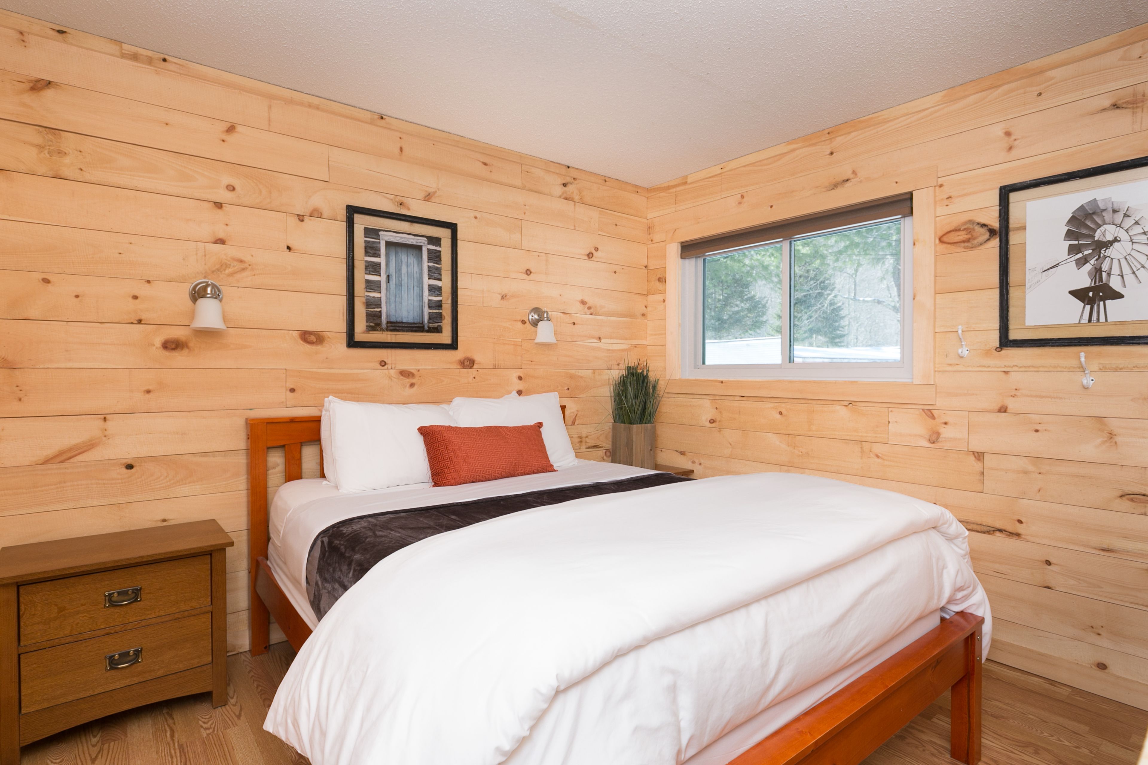 Ein schlafzimmer mit Holzwänden, einem Bett, Nachttischen, einem Fenster und Wandleuchten.