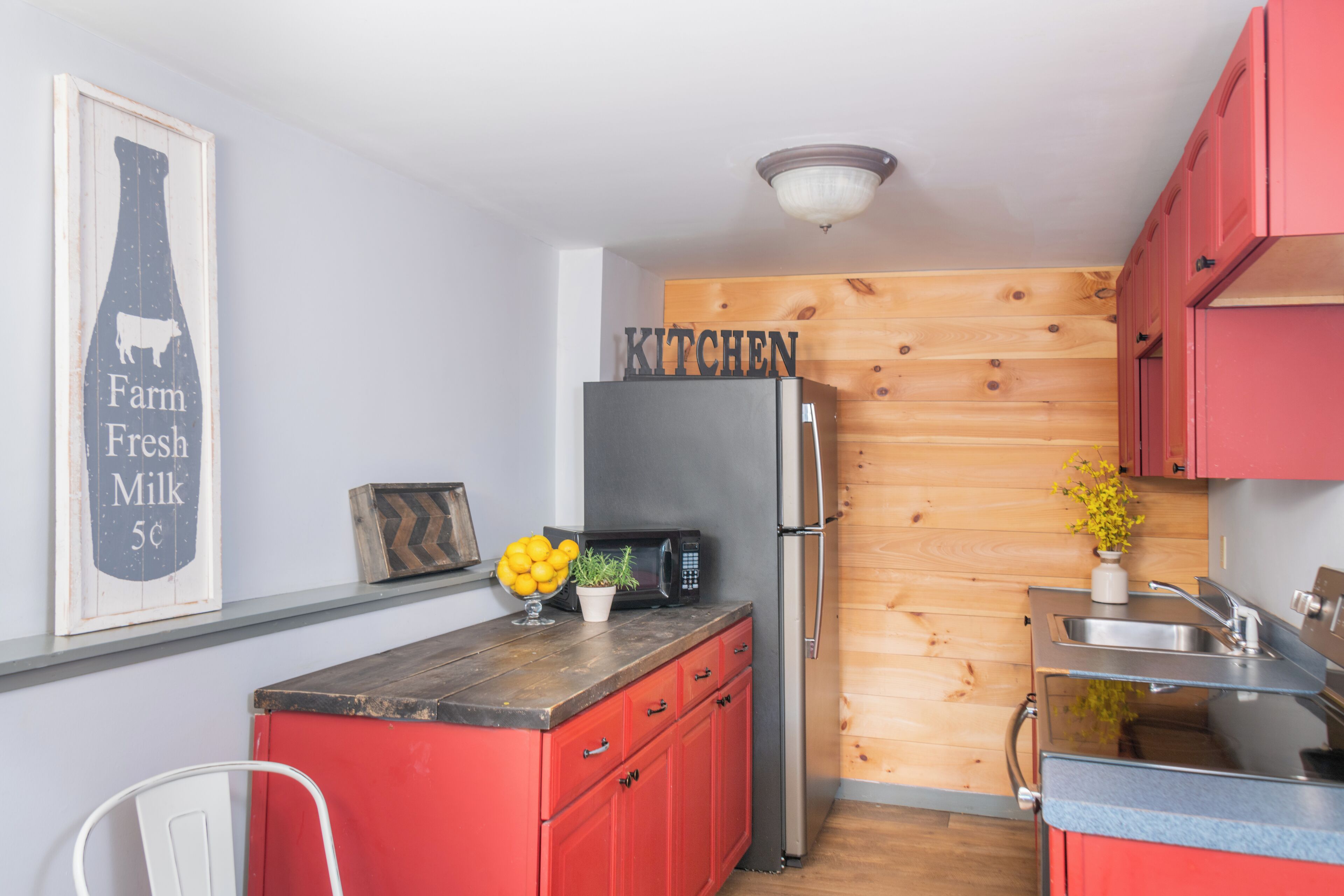 Cocina compacta con armarios rojos, un refrigerador de acero inoxidable, un microondas y una pared de acento de madera.
